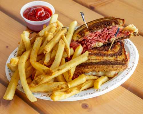 A plate of crispy French fries next to a grilled sandwich filled with sliced meat, served with a side of ketchup.