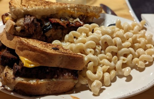 A hearty sandwich with grilled meat and cheese, served with a side of macaroni pasta.