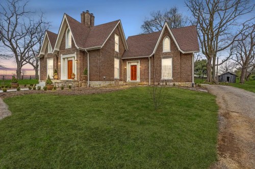 A charming brick house with a gabled roof, surrounded by a lush lawn and trees, at dusk.