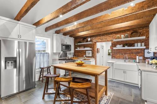 Modern kitchen with exposed wooden beams, brick walls, stainless steel appliances, and a wooden island with stools.