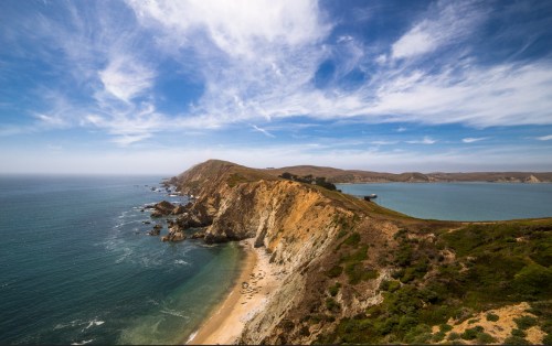 A scenic coastal view featuring cliffs, sandy beaches, and a clear blue sky over the ocean.