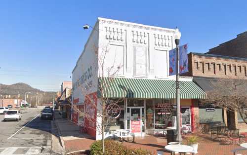 A street view of a small town with a vintage storefront, green awning, and nearby trees under a clear blue sky.