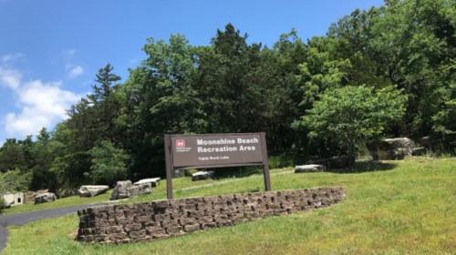 Sign for Moonshine Beach Recreation Area at Table Rock Lake, surrounded by green trees and a clear blue sky.