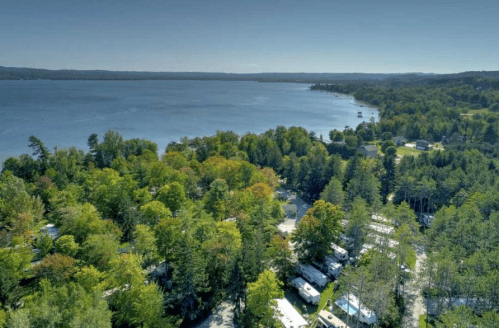 Aerial view of a serene lake surrounded by lush greenery and a campsite with RVs along the shoreline.