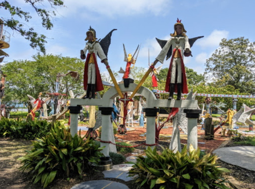 Colorful sculptures of angels and figures in a vibrant outdoor garden setting with greenery and blue skies.