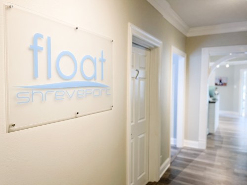 Sign for "float shreveport" on a wall in a well-lit hallway with doors on either side.