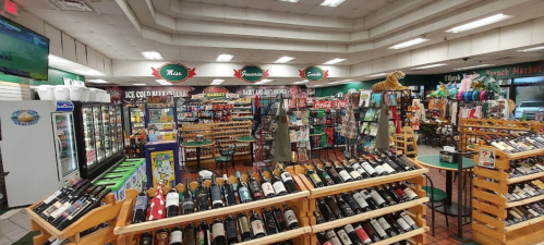 A spacious market interior with shelves of wine, snacks, and drinks, featuring colorful displays and a sports screen.