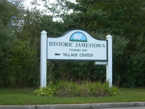 Sign for Historic Jamestown, founded in 1678, with an arrow pointing left to the Village Center, surrounded by greenery.