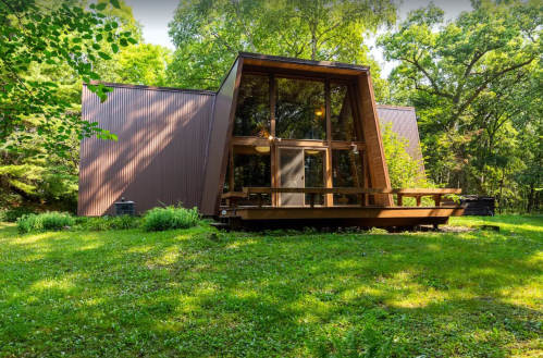 A modern A-frame house surrounded by greenery, featuring large windows and a wooden deck.