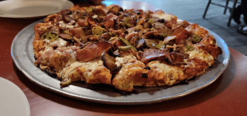 A freshly baked pizza topped with pepperoni, mushrooms, and jalapeños on a metal serving tray.