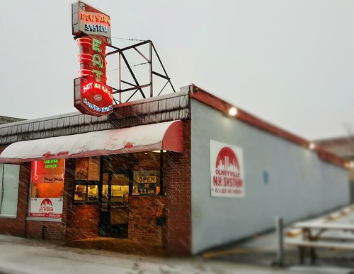 A diner with a neon sign reading "Eat" and "Open at 11 AM," surrounded by snow on a winter day.