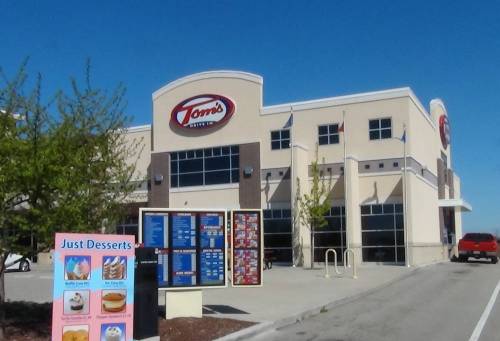 Exterior of Tom's restaurant with a dessert menu sign in front and a clear blue sky.