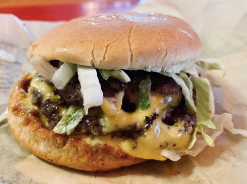 A close-up of a juicy cheeseburger with lettuce and onions on a soft bun, resting on a piece of parchment paper.