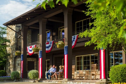 A cozy porch decorated with red, white, and blue bunting, featuring two people sitting and enjoying the view.