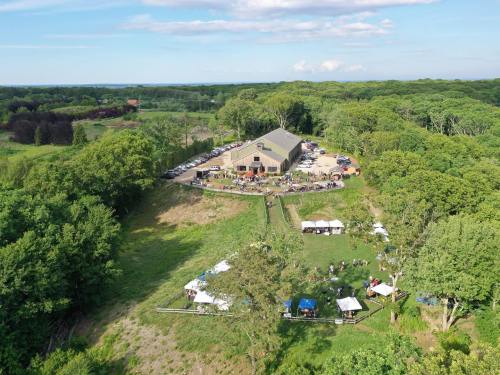 Aerial view of a large gathering at a venue surrounded by trees, with tents and cars parked nearby.