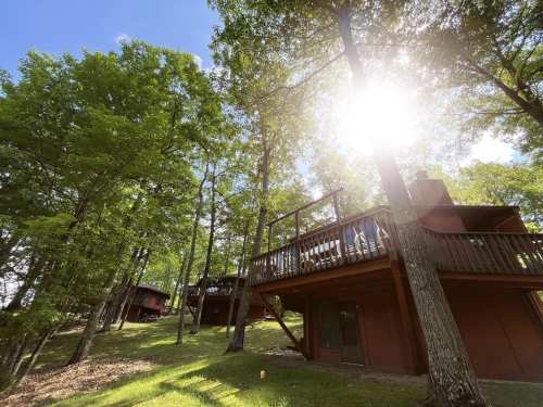Sunlight filters through trees, illuminating rustic cabins on a hillside surrounded by lush greenery.