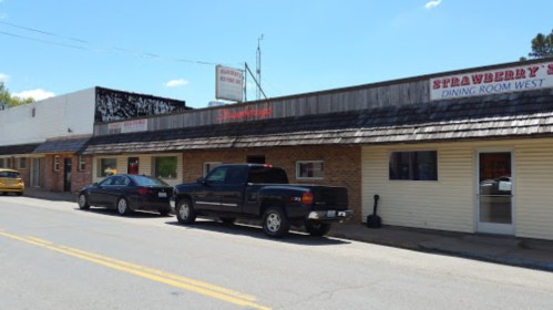 A small town street featuring a restaurant and parked cars under a clear blue sky.