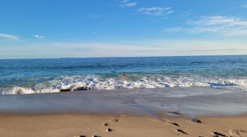 A serene beach scene with gentle waves lapping at the shore under a clear blue sky.