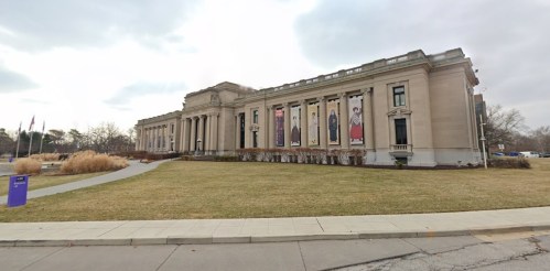 A large, classical-style museum building with banners on the facade, surrounded by a grassy area and pathways.