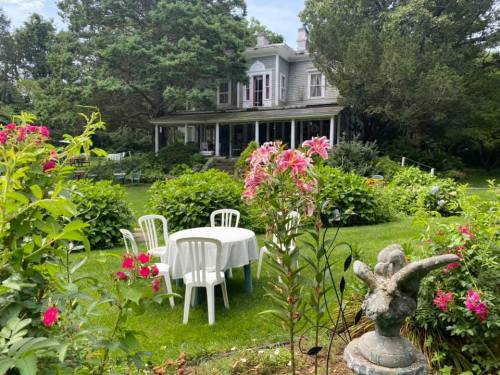 A charming garden scene featuring a table and chairs surrounded by flowers, with a house in the background.