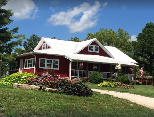 A charming red house with a white roof, surrounded by colorful flowers and greenery on a sunny day.