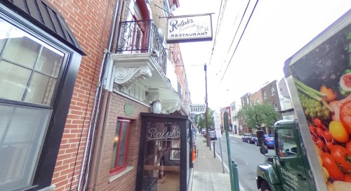 View of Ralph's Restaurant with a sign, located on a street lined with brick buildings and greenery.
