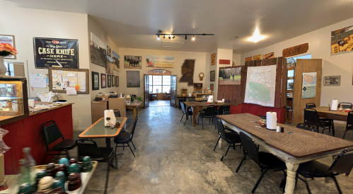A spacious room with tables and chairs, featuring rustic decor, maps, and various wall art. Brightly lit and inviting.