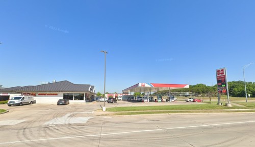 A gas station with a convenience store, surrounded by cars, under a clear blue sky.