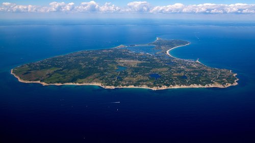 Aerial view of a lush green island surrounded by blue ocean and dotted with boats and coastal features.