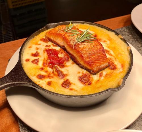 A cast-iron skillet with creamy baked dish topped with a piece of salmon and garnished with rosemary.