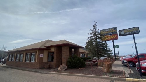A brick building with a sloped roof, featuring signs and a parking lot, under a cloudy sky.