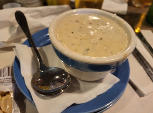 A bowl of creamy soup with herbs, served on a blue plate with a spoon, placed on a table with napkins.