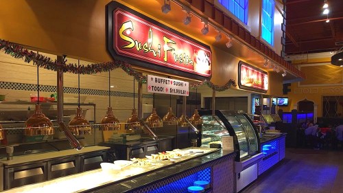 Interior of a sushi restaurant featuring a buffet setup with illuminated signs and decorative garlands.
