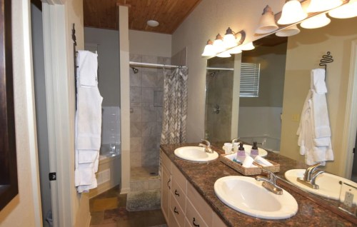 A modern bathroom featuring dual sinks, a shower, and a bathtub, with light-colored walls and wooden accents.