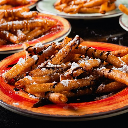 A close-up of crispy fried dough sticks drizzled with chocolate and dusted with powdered sugar on colorful plates.
