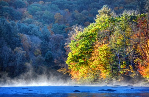 A serene river scene with colorful autumn trees and mist rising from the water, surrounded by lush forest.