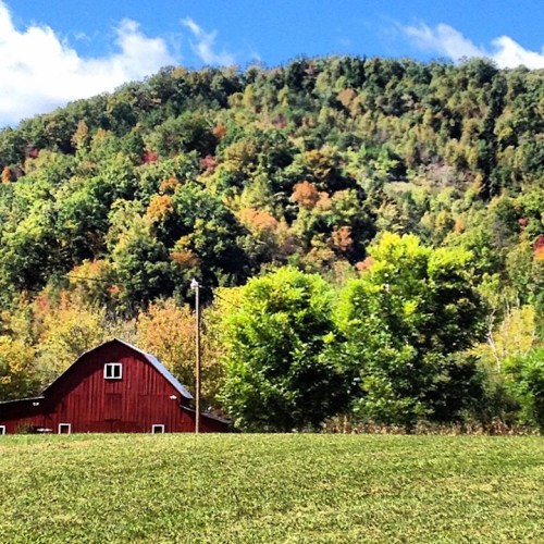 A red barn sits in a green field, surrounded by colorful autumn trees and a blue sky with fluffy clouds.