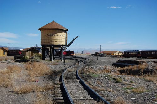 A vintage water tower beside railway tracks in a desert landscape under a clear blue sky.