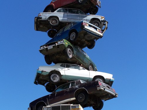 A stack of seven old cars piled high against a clear blue sky.