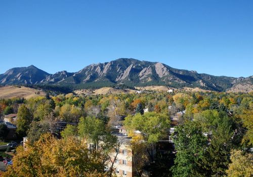 A scenic view of mountains with colorful autumn trees and clear blue skies in Boulder, Colorado.