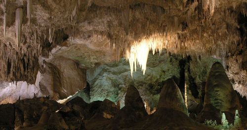 A stunning cave interior featuring stalactites and stalagmites, illuminated by soft, colorful lighting.