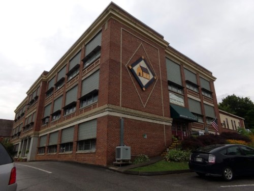 Brick building with decorative diamond design, featuring multiple windows and a sign for a business. Parking area visible.