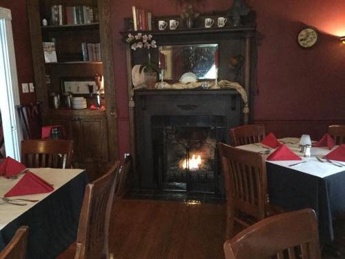 Cozy dining room with wooden tables, red napkins, and a fireplace surrounded by bookshelves and decor.