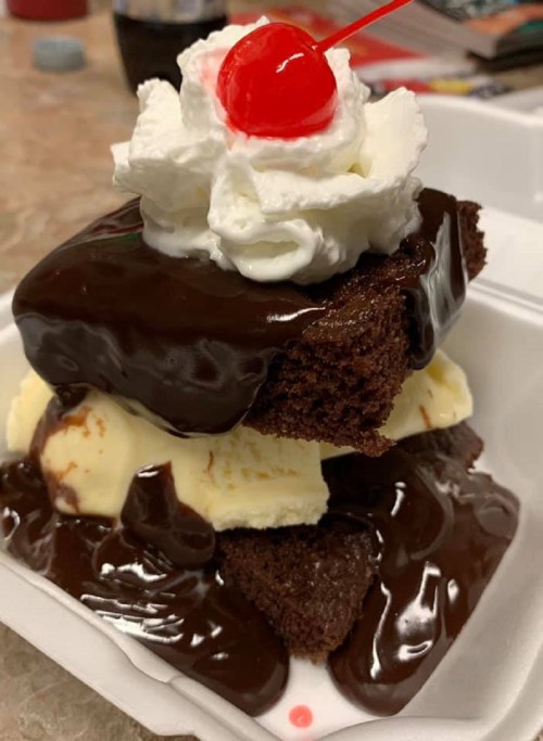 A decadent dessert with layers of chocolate cake, vanilla ice cream, chocolate sauce, whipped cream, and a cherry on top.