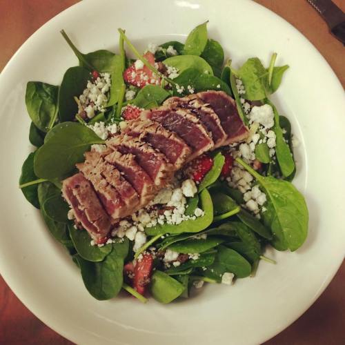 A fresh salad with spinach, strawberries, feta cheese, and sliced seared tuna on top.