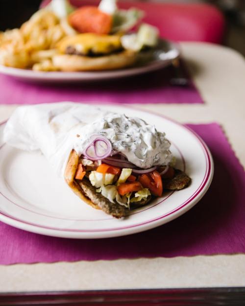 A wrapped sandwich filled with vegetables and sauce on a plate, with a burger and fries in the background.