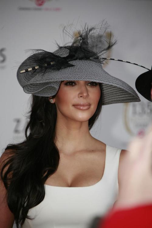 A woman in a stylish hat poses for a photo, wearing a white dress and smiling at the camera.