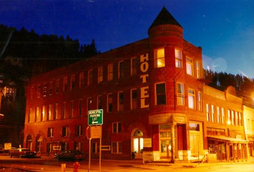 Historic brick hotel at dusk, with illuminated windows and a sign reading "HOTEL," surrounded by trees.