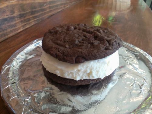 A chocolate cookie sandwich filled with vanilla ice cream, resting on a silver foil plate.