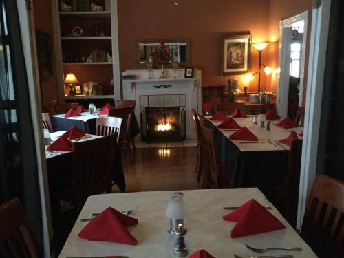Cozy restaurant interior with tables set for dining, red napkins, and a fireplace glowing in the background.